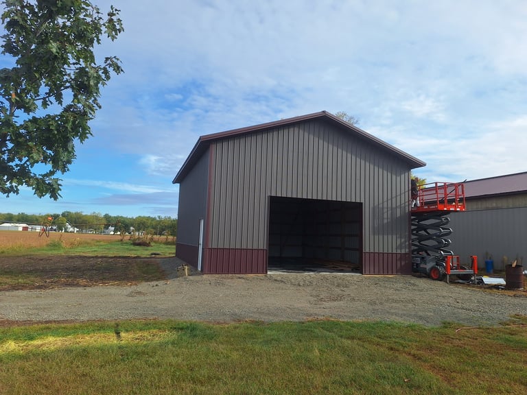 Dark metal agricultural barn with open garage door on rural farm property with equipment and machinery nearby