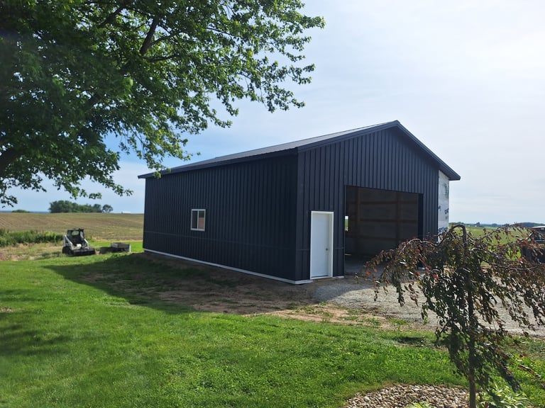 Black metal agricultural barn with white trim in rural setting surrounded by green fields and trees