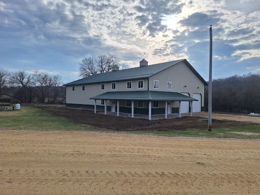 White wooden barn with covered porch and tall chimney on rural property under cloudy sky