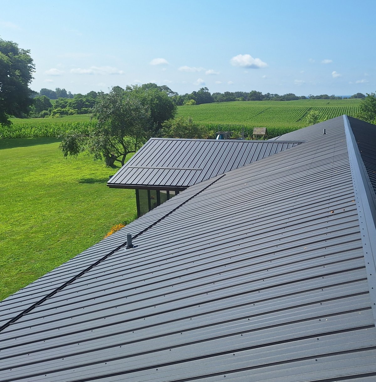 Modern metal-roofed building overlooking rural farmland with green fields and scattered trees under blue sky